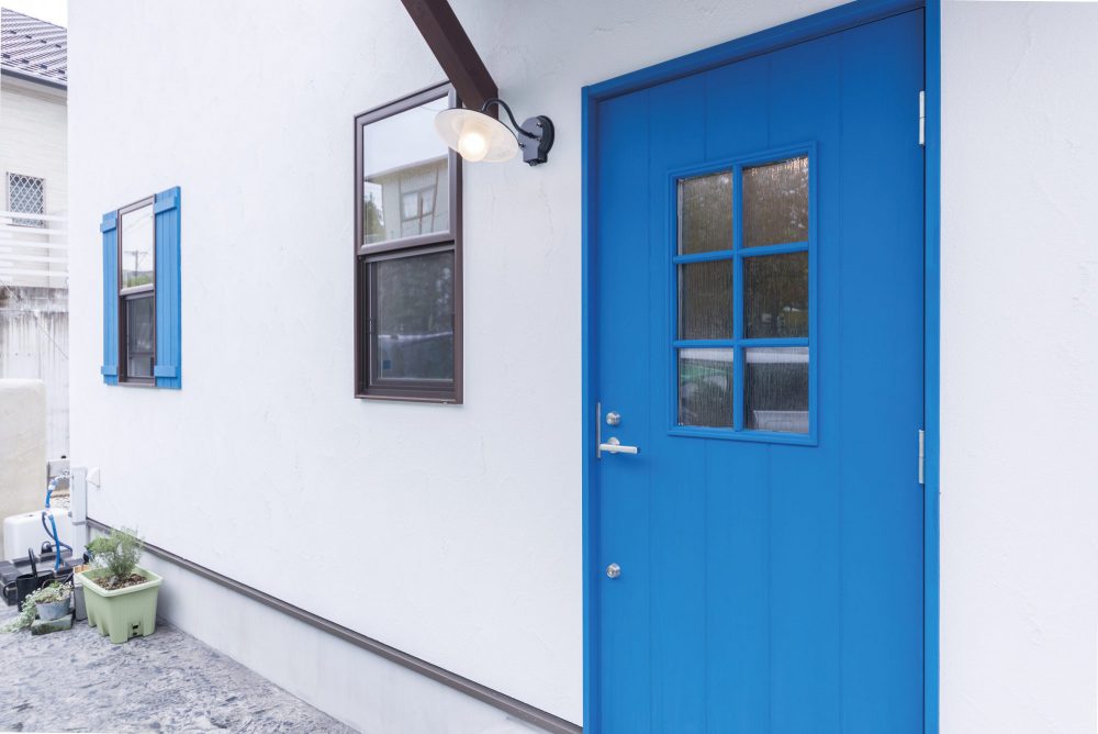 白の塗り壁に映えるナチュラルカントリーなブルーの玄関ドア 住宅外観